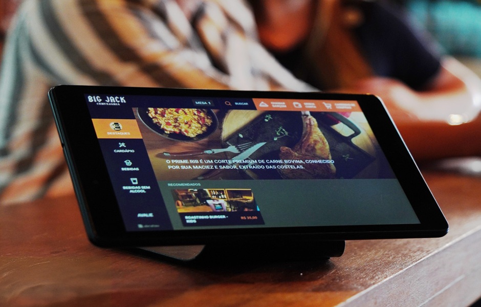 Pessoa usando tablet com menu digital do Big Jack, restaurante especializado em cortes de carne bovina, servido em um ambiente aconchegante.