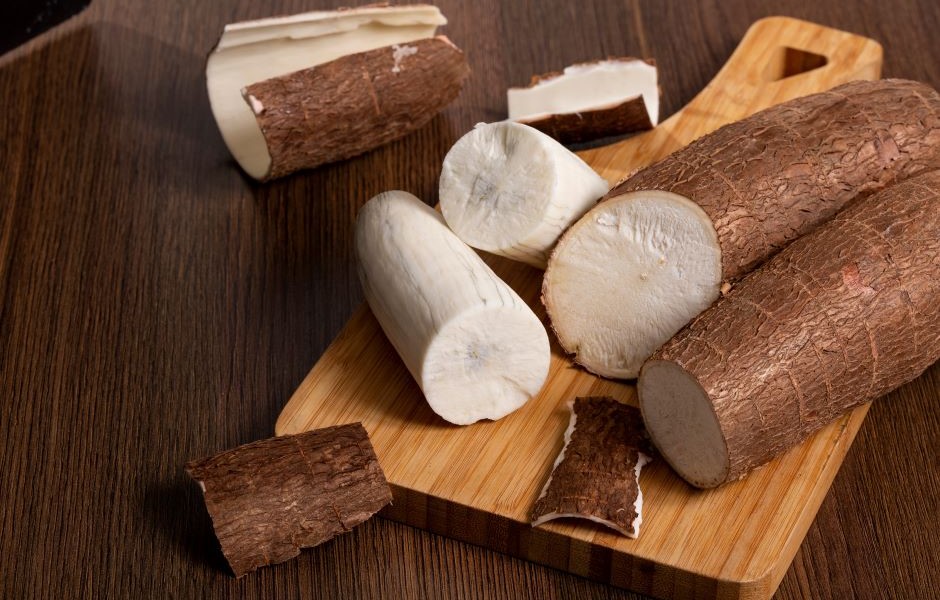 Batata-doce branca cortada ao meio e ao lado de uma batata-doce roxa em um acabamento rústico, dispostas em uma tábua de madeira sobre uma superfície de madeira escura, ideal para alimentação saudável e receitas nutritivas com batata-doce.
