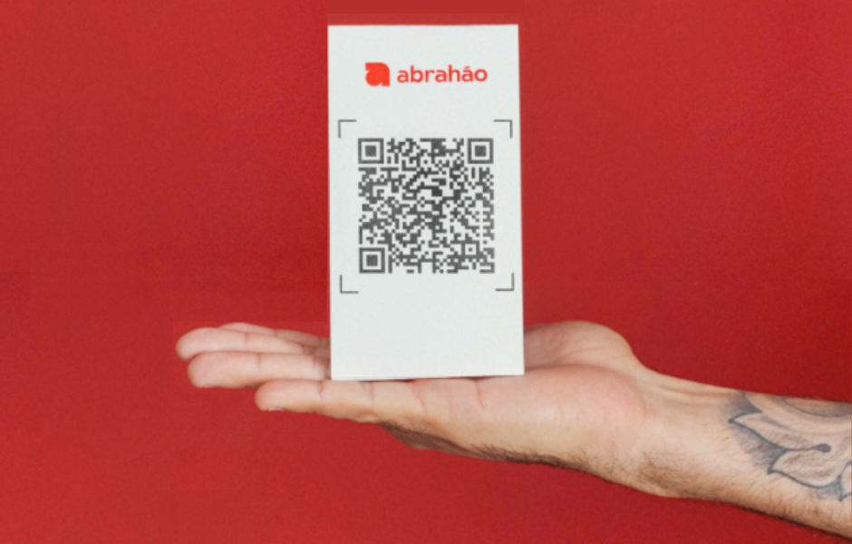 Pessoa segurando um cartão de visita com código QR, logo da abrahao e fundo vermelho, destacando a tecnologia de pagamento ou informações digitais.