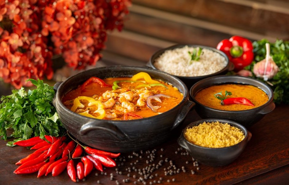 Prato de comida típica indiana com vários molhos, arroz branco, temperos e ingredientes frescos ao redor em uma mesa de madeira, representando a culinária da Índia.