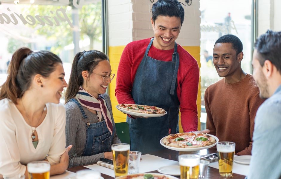 Grupo de amigos em uma pizzaria, sorrindo e apreciando pizzas artesanais, em uma atmosfera alegre e descontraída, ideal para momentos de lazer com amigos.